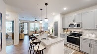This thoughtfully designed single-floor residence offers a cohesive open-concept layout that seamlessly connects the kitchen, dining, and living areas. The kitchen is a standout feature, showcasing gray shaker-style cabinetry, a subway tile backsplash, stainless steel appliances including a refrigerator, range, and microwave, and a granite-topped island with an undermount sink and bar seating — ideal for casual dining and entertaining. Stylish globe pendant lights hang above the island, adding a contemporary touch.

The living room is bright and welcoming, benefiting from natural light through large windows and a glass door that opens to the outdoors. A ceiling fan overhead and wood-look plank flooring throughout the main living areas contribute to a clean, modern aesthetic.

The bedroom offers a comfortable, carpeted retreat with ample wall space and access to the dedicated closet. The bathroom is well-appointed with a vanity featuring blue-gray cabinetry, granite countertops, wood-look flooring, and a tub-shower combination with marble-style tile surround. The layout ensures convenient access between the bathroom and bedroom, creating a functional and cohesive private living zone.