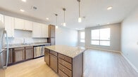 Located at 11848 Templeton Ct in Omaha, Nebraska, this well-designed one-bedroom, two-bathroom residence offers a thoughtful layout with modern finishes throughout. The open-concept kitchen and living area serves as the heart of the home, anchored by a large center island topped with granite countertops and illuminated by three stylish pendant lights. The kitchen is equipped with a full suite of stainless steel appliances, including a refrigerator, range, microwave, and dishwasher, complemented by a two-tone cabinetry design featuring white upper cabinets and rich dark lower cabinets. Light hardwood flooring flows seamlessly through the kitchen and living area, which benefits from generous natural light through large windows. The spacious bedroom features plush carpeting, a ceiling fan, a walk-in closet with built-in shelving, and a bright window. Both bathrooms are finished with granite-topped dark wood vanities and tile-style flooring, with one bathroom featuring a full tub-shower combination. A hallway area conveniently houses a stacked in-unit washer and dryer. Neutral gray tones and recessed lighting throughout give the space a clean, contemporary ambiance.