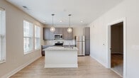 This single-floor, one-bedroom, one-bathroom unit at 800 E Long Street in Columbus, Ohio offers a thoughtfully designed layout that maximizes its compact footprint. The open-concept kitchen serves as the centerpiece of the living area, featuring gray shaker-style cabinetry, granite-look countertops, a subway tile backsplash, and a full suite of stainless steel appliances including a range, over-the-range microwave, and refrigerator. A central kitchen island with a built-in sink and pendant globe lighting above adds both functionality and style. Light wood-look flooring runs throughout the main living areas, contributing to a bright, clean aesthetic complemented by natural light from multiple windows with blinds.

A narrow hallway with recessed and flush-mount ceiling lighting connects the main living area to the private bedroom and bathroom. The bedroom is carpeted and finished in neutral tones, offering a quiet retreat, with direct access to the bathroom. The bathroom includes a gray vanity with granite-look countertop, a walk-in glass-door shower with built-in shelving, and wood-look tile flooring that ties the space together. A dedicated closet completes the unit, providing organized storage within this efficiently designed home.