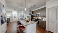 This thoughtfully designed 2-bedroom, 2-bathroom residence offers a seamless single-floor layout that maximizes comfort and functionality. The open-concept kitchen and dining area serves as the heart of the home, showcasing granite countertops, a large center island with bar seating, rich dark wood cabinetry, a stacked tile backsplash, and a full suite of stainless steel appliances. Stylish pendant lighting illuminates the island, adding a modern touch to the space. Rich hardwood-style flooring flows throughout the main living areas, complementing the contemporary aesthetic. The living room is bright and airy, featuring soaring ceilings, a ceiling fan, and sliding glass doors that open to a private outdoor patio with pleasant exterior views. Both bedrooms are carpeted and generously sized, each featuring ceiling fans and large windows that invite abundant natural light. The primary bathroom is elegantly finished with granite countertops, dark wood vanity cabinetry, tile flooring, and a soaking tub with tile surround. A walk-in closet with built-in wire shelving provides ample storage. A dedicated dining nook and a convenient hallway round out this well-organized floor plan, making this residence as practical as it is stylish.