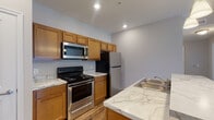 Located at 941 Taylor Station Rd in Gahanna, Ohio, this single-floor residence offers a well-designed, open-concept layout that balances functionality with modern finishes throughout. The kitchen is a standout feature, equipped with a full suite of stainless steel appliances including a refrigerator, range, and over-the-range microwave. Warm honey-toned shaker-style cabinetry extends to the ceiling, providing generous storage, while marble-look countertops add a polished aesthetic. A central kitchen island with seating overhang and pendant lighting above serves as a natural gathering point, seamlessly connecting the kitchen to the main living area. The living room is bright and open, featuring a ceiling fan with light fixture, plush carpeting, and a set of French doors that lead to an outdoor balcony, filling the space with natural light. Durable hardwood-style flooring runs through the kitchen and entry areas, transitioning to carpet in the living and bedroom spaces. The bedroom includes a closet with wire shelving and connects to additional storage. The bathroom is clean and functional, featuring a tub-shower combination, a marble-look vanity countertop, warm wood cabinetry, and hardwood-style flooring. Recessed lighting throughout the unit ensures consistent, even illumination in every room.