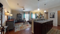 This thoughtfully designed single-floor residence offers a comfortable and cohesive living experience across one bedroom and one bathroom. Rich hardwood-style flooring flows throughout the main living areas, complemented by crown molding that adds a refined architectural detail throughout the home.

The open-concept layout seamlessly connects the kitchen, dining, and living areas. The kitchen features dark espresso cabinetry, granite countertops, a kitchen island with a double sink, pendant lighting, and black appliances including a range and built-in microwave. A spacious entryway with a closet provides convenient storage upon arrival.

The living room is bright and welcoming, with multiple windows dressed in teal curtains that invite natural light. A ceiling fan adds comfort, and the space flows naturally into a dedicated dining area, which features its own window and access to a patio or balcony through vertical blinds.

The bedroom is a calm, carpeted retreat with crown molding, a ceiling fan, natural light from a window, and ample space for furnishings. The full bathroom includes a tiled tub-shower combination, a vanity with countertop storage, and hardwood-style flooring. A walk-in closet adjacent to the bedroom provides generous storage. This residence offers a functional and well-appointed layout with consistent finishes throughout.