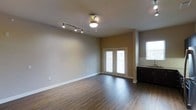 Located in Carrollton, this single-floor space offers a clean, functional layout with thoughtful design details throughout. The main living area is highlighted by rich, dark hardwood-style flooring that runs the length of the room, providing a warm and polished aesthetic. A combination of track lighting and a ceiling light fixture ensures the space is well-lit, offering both ambient and directional illumination. Neutral-toned walls complement the flooring and contribute to a bright, open atmosphere. A set of classic French doors serves as a focal point, allowing natural light to pour into the living area while providing access to the exterior. Additional windows further enhance the natural light, creating an airy and inviting environment. Adjacent to the main living space, a dark-cabinetry wet bar or kitchenette area adds a practical touch, featuring contrasting countertops that stand out against the cabinetry. White baseboards frame the room cleanly, adding a crisp finishing detail throughout. The overall layout is open and versatile, well-suited for a variety of uses. The combination of modern finishes and classic architectural elements gives this Carrollton space a balanced and welcoming character.