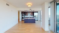 Located at 408 W 5th St in the heart of Uptown Charlotte, this high-rise residence offers a compelling combination of contemporary design and panoramic city views. Floor-to-ceiling glass walls span multiple rooms, flooding the space with natural light and framing expansive vistas of the Charlotte skyline and surrounding cityscape.

The open-concept living and kitchen area is anchored by light hardwood flooring that enhances the sense of space. The gourmet kitchen is outfitted with rich dark cabinetry, granite countertops, a mosaic tile backsplash, stainless steel appliances including a double wall oven and built-in refrigerator, and a large center island with a navy-blue base. A balcony is directly accessible from this living area, offering outdoor space with striking skyline views.

The carpeted bedroom features its own floor-to-ceiling window wall with a ceiling fan overhead, providing sweeping views of the surrounding neighborhoods. An additional carpeted room offers flexible use as a bedroom or office. The bathroom presents a clean, minimalist aesthetic with large-format tile flooring, a deep soaking tub, and a glass-enclosed shower. The overall ambiance is modern and refined, ideal for urban living.