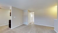 This single-floor residence offers a clean, understated aesthetic defined by neutral tones and practical design throughout. The bedroom is a standout feature, showcasing wall-to-wall carpeting in a warm beige hue that adds a sense of comfort and warmth underfoot. Smooth, light-colored walls complement the soft flooring, creating a cohesive and calming atmosphere throughout the space. A louvered bi-fold closet door provides ample storage while contributing a classic architectural detail to the room. HVAC vents are thoughtfully integrated into both the upper wall and the floor, ensuring efficient climate control throughout the year. White baseboards frame the perimeter of the room, offering a crisp contrast against the neutral walls and carpet. An open doorway leads to an adjacent area that benefits from natural light streaming in through a window, suggesting a bright and connected layout. The overall design is simple yet functional, with a neutral palette that offers versatility for a variety of furnishing styles. This space presents a well-maintained, move-in-ready environment suited for comfortable everyday living.