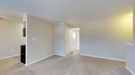 This single-floor residence offers a clean, understated aesthetic defined by neutral tones and practical design throughout. The bedroom is a standout feature, showcasing wall-to-wall carpeting in a warm beige hue that adds a sense of comfort and warmth underfoot. Smooth, light-colored walls complement the soft flooring, creating a cohesive and calming atmosphere throughout the space. A louvered bi-fold closet door provides ample storage while contributing a classic architectural detail to the room. HVAC vents are thoughtfully integrated into both the upper wall and the floor, ensuring efficient climate control throughout the year. White baseboards frame the perimeter of the room, offering a crisp contrast against the neutral walls and carpet. An open doorway leads to an adjacent area that benefits from natural light streaming in through a window, suggesting a bright and connected layout. The overall design is simple yet functional, with a neutral palette that offers versatility for a variety of furnishing styles. This space presents a well-maintained, move-in-ready environment suited for comfortable everyday living.