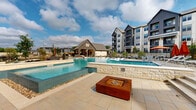 Located at 3900 Robinson Rd in Grand Prairie, Texas, this modern residential community offers an impressive array of outdoor amenities designed for resort-style living. The complex showcases a striking architectural design that blends board-and-batten siding, stone accents, dark metal roofing, and warm wood detailing across its multi-story buildings — creating a refined yet approachable aesthetic throughout.

At the heart of the community is a generously sized swimming pool with crystal-clear blue water, surrounded by a spacious sun deck furnished with lounge chairs and shaded umbrellas, ideal for relaxing or socializing. Adjacent to the main pool is a dedicated spa or wading pool, elegantly framed in natural stone with a central fire feature, offering a more intimate outdoor retreat.

The amenity grounds also include a well-maintained putting green, providing residents with a unique recreational outlet set amid thoughtfully landscaped surroundings. Native plantings, ornamental grasses, decomposed granite, and natural boulders are woven throughout the outdoor spaces, creating a cohesive and low-maintenance landscape design.

A covered outdoor gathering area with seating and grilling stations adds further versatility to the amenity deck. The multi-story residential buildings frame the courtyard, with private balconies overlooking the lush grounds below, reinforcing the community's commitment to both style and livability.