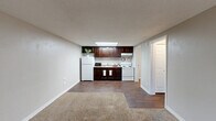 Located at 4941 Central Drive in Stone Mountain, GA, this one-bedroom, one-bathroom unit offers a practical and efficiently designed single-floor layout. The open-concept living area flows seamlessly into the kitchen, which features rich dark-brown cabinetry, white appliances including a refrigerator and range, and a skylight that brings in natural overhead light. The transition from carpet in the living area to wood-style flooring in the kitchen creates a clear and functional delineation between the two spaces. Neutral gray walls and a textured ceiling run throughout, lending a clean, understated aesthetic. The front entry leads into the carpeted living room, which receives natural light through a window with blinds. The bedroom is a comfortable, well-proportioned space with plush carpet, a ceiling fan with light fixture, a window overlooking greenery, and a dedicated closet with built-in shelving and hanging rods for organized storage. The bathroom is finished with a white vanity and countertop, wood-style flooring, a large mirror, and a full tub-and-shower combination with a curtain rod. A hallway connects the main living areas to the bedroom and bathroom, providing a logical and private flow throughout the unit.