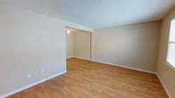 This single-floor 1-bedroom, 1-bathroom unit offers a generous and functional layout throughout. Warm-toned hardwood-style flooring runs consistently across the living, dining, and bedroom areas, creating a cohesive and easy-to-maintain interior. Textured ceilings are present throughout the main living spaces, adding subtle dimension overhead.

The living area is open and well-proportioned, with neutral beige walls and clean white baseboards. A wide archway connects the living space to a dedicated dining area, which features a ceiling fan with a light fixture. This dining space flows directly into the kitchen, visible through a pass-through opening.

The kitchen is efficiently designed with white shaker-style cabinetry, stone-look countertops, a double stainless steel sink, a range, and a dishwasher. A skylight overhead brings in natural light, brightening the workspace.

The bedroom is a comfortable size with a ceiling fan, a window allowing natural light, and the same hardwood-style flooring found throughout.

The bathroom is clean and straightforward, featuring a full tub-shower combination with white tile surround, a toilet, and a vanity. Grab bars are installed along the walls, adding a practical accessibility feature to the space.