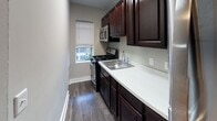 This single-floor residence offers a thoughtfully designed layout that balances functionality and comfort. The living area is a standout feature, showcasing gleaming hardwood floors that extend throughout the main spaces, complemented by neutral gray walls and multiple windows that flood the room with natural light. An elegant arched doorway connects the living area to the kitchen, adding a classic architectural touch to the open flow of the space.

The kitchen is designed for practicality, featuring rich dark wood cabinetry that extends to the upper walls, providing generous storage. Stainless steel appliances, including a refrigerator, gas range, and over-the-range microwave, are seamlessly integrated alongside a double-basin sink set into clean white countertops. A window above the range brings in additional natural light.

The bedroom continues the hardwood flooring and neutral palette, with two windows offering views to the outside and allowing ample daylight to fill the room.

The bathroom is a refined space finished with large-format marble-style tiles on both the floors and the tub surround. A soaking tub with a sliding glass panel, a classic cast-iron radiator, and a dark wood vanity with a white countertop complete this well-appointed room. Natural light enters through a frosted window, enhancing the clean, bright aesthetic.