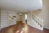 This two-story home at 4800 Lamonte Lane in Houston, TX offers a practical and well-organized layout across two floors. The main level features a combined dining and living area with warm hardwood-style flooring, neutral beige walls, and natural light streaming through large windows with blinds. A standout built-in shelving unit divides the living area from the kitchen, adding both character and storage. The kitchen is well-appointed with dark cabinetry, a classic white subway tile backsplash, stainless steel appliances including a refrigerator and electric range, a double sink, and a peninsula that opens toward the living space. A pantry and utility room provide additional storage and functionality on this floor. A carpeted staircase leads to the upper level, where the generously sized primary bedroom features soft carpet flooring, a ceiling fan with light fixture, and a window allowing natural light. The upper floor also includes a closet and bathrooms. Three bathrooms are distributed throughout the home, including one with a tiled tub/shower combination and hardwood-style flooring. The overall ambiance is clean, neutral, and move-in ready, offering efficient use of space throughout.