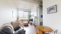 Located at 200 S 8th St in Richmond, Indiana, this 2-bedroom, 1-bathroom residence showcases a distinctive industrial loft character defined by whitewashed wood plank ceilings, exposed ductwork, and oversized grid-pane windows that flood the interior with abundant natural light. The open living and dining area serves as the heart of the home, featuring durable hardwood-style flooring, soaring ceiling height, and a bright, airy ambiance framed by large windows overlooking the surrounding neighborhood. The galley-style kitchen is efficiently designed with light wood cabinetry, ample counter space, and full appliances including a range, refrigerator, dishwasher, and built-in microwave. The spacious primary bedroom offers a generous footprint with large grid windows providing sweeping outdoor views, while a ceiling fan adds comfort. The second bedroom maintains the loft aesthetic with tall ceilings, hardwood-style floors, and a prominent window that brings in natural light. A central hallway with light maple doors connects the rooms seamlessly. Four closets throughout the unit provide excellent storage. The space blends urban industrial design with warm, livable interiors, creating a unique and character-rich home in the heart of Richmond.