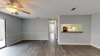 This single-story home offers a well-organized layout with consistent finishes throughout. The open living and dining area is anchored by rich wood-look flooring and neutral gray walls, creating a clean, cohesive aesthetic. A ceiling fan provides comfort overhead, while a pass-through window connects the living space to the kitchen, enhancing the sense of openness. The galley-style kitchen is efficiently designed, featuring white cabinetry, dark granite-look countertops, a tile backsplash, and white appliances including a refrigerator and range. A central hallway connects the main living areas to the private quarters of the home. The bedrooms are generously sized, each equipped with ceiling fans, wood-look flooring, and windows that allow natural light to filter in. One bedroom features direct access to a bathroom and includes a sliding closet door. The bathrooms are finished with white cabinetry, dark countertops, large vanity mirrors with overhead lighting, and wood-look flooring. One bathroom includes a full tub-shower combo with tile surround. A textured ceiling is present throughout the home, adding a classic touch to the overall design.