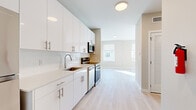 This thoughtfully designed single-floor unit makes efficient use of its space with a clean, modern aesthetic carried consistently throughout. Light hardwood flooring flows seamlessly across all areas, contributing to a bright, cohesive feel.

The kitchen is a standout feature, outfitted with high-gloss white cabinetry extending to the ceiling, white quartz countertops, and a classic subway tile backsplash. Stainless steel appliances — including a range, dishwasher, microwave, and refrigerator — provide a full suite of functionality. The sink is positioned along the counter run, and the layout opens directly toward the main living area, which is bathed in natural light from large windows overlooking the surrounding neighborhood.

The living area benefits from multiple windows fitted with roller shades, allowing for adjustable natural light throughout the day. The warm, neutral wall tones complement the light flooring and create an inviting ambiance.

The bathroom is finished to a high standard, featuring floor-to-ceiling marble-look tile, a soaking tub with a combination shower, and matte black hardware accents that add a modern contrast to the bright white palette.

Entry to the unit is through a solid, paneled door with a smart lock, adjacent to the kitchen. A closet and hallway provide practical storage and circulation. Overall, the space presents a polished, move-in ready environment with thoughtful finishes throughout.