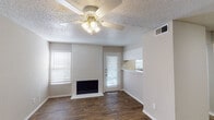 This single-floor residence offers a functional and well-appointed layout across several distinct areas. The living room serves as the heart of the home, anchored by a painted brick fireplace that adds warmth and character to the space. Rich wood-look flooring runs throughout the main living areas, complemented by a ceiling fan with a light fixture overhead and a textured popcorn ceiling. Natural light filters in through blinds-covered windows, and a glass-panel door provides access to the outdoors. A convenient pass-through opening connects the living area to the kitchen, which features white cabinetry and a practical countertop workspace. The bedroom is carpeted for comfort, with a large window that brings in additional natural light and neutral walls that create a calm, versatile atmosphere. The bathroom is clean and efficiently designed, featuring a full tub and shower combo with tiled surround, a toilet, white overhead cabinetry for storage, and a vanity topped with a speckled countertop and a framed mirror. An entry area with wood-look flooring and a paneled front door rounds out the layout. Throughout the space, a consistent neutral color palette and clean finishes provide a move-in-ready environment.
