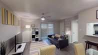This one-bedroom, one-bathroom unit is laid out across a single floor, offering a functional and cohesive living experience. The living room serves as the heart of the space, featuring wood-style flooring, a ceiling fan with integrated lighting, and a large sliding glass door dressed with vertical blinds that allows natural light to fill the room. The open sightlines create an inviting atmosphere well-suited for both relaxing and entertaining.

The kitchen is designed for efficiency, with a galley-style layout featuring white cabinetry, granite-look countertops, and black appliances including a range, refrigerator, and dishwasher. A window above the sink area provides additional natural light.

The bedroom is generously proportioned, with wood-style flooring continuing throughout, a window with blinds, and ample room for furnishings. The bathroom includes a tub-shower combination with overhead cabinetry for storage.

Throughout the unit, a consistent neutral gray color palette ties each space together, complemented by warm wood-tone flooring. The overall ambiance is clean, modern, and functional, making it a practical and comfortable single-floor residence.