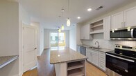 Located at 305 Oberlin Rd in Raleigh, NC, this single-floor residence offers a thoughtfully designed open-concept layout with modern finishes throughout. The kitchen serves as a central highlight, featuring white shaker-style cabinetry, granite countertops, a herringbone-patterned tile backsplash, and a large center island with built-in shelving and pendant lighting above. Stainless steel appliances — including a side-by-side refrigerator with ice and water dispenser, electric range, built-in microwave, and dishwasher — complete this well-appointed space. Hardwood-style flooring flows throughout the main living areas, adding warmth and continuity to the open floor plan. The living area is bright and airy, enhanced by a ceiling fan and sliding glass doors that open to a private balcony, inviting natural light and outdoor views. The bedroom features plush carpeting and neutral wall tones, creating a calm and comfortable retreat. The bathroom is finished with granite countertops, a tiled soaking tub and shower combination, hardwood-style flooring, and direct access to a spacious walk-in closet with built-in shelving and hanging rods. Clean lines, recessed lighting, and a cohesive neutral palette give the entire space a polished, contemporary feel.
