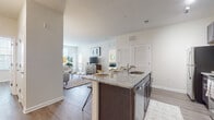 This single-story residence offers a thoughtfully designed open-concept layout that seamlessly connects the kitchen and living areas. The kitchen is a standout feature, equipped with dark espresso cabinetry, granite countertops, stainless steel appliances including a range, microwave, and refrigerator, and a large island with bar seating and an integrated sink. Track lighting illuminates the workspace, while wood-style plank flooring runs throughout the main living areas.

The living room is bright and welcoming, benefiting from multiple windows that invite generous natural light. A private entry door with glass paneling adds an additional source of light to the sitting area. The space flows naturally into a comfortable seating arrangement, making it ideal for everyday living.

The primary bedroom is a serene retreat with wood-style flooring and windows providing ample natural light. An additional bedroom offers similar warmth and simplicity. Two bathrooms serve the residence: one full bath with dark vanity cabinetry, a glass-enclosed shower, and tile flooring, and a separate water closet with tile flooring. Neutral tones, clean lines, and consistent finishes create a cohesive and modern ambiance throughout.