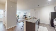 This single-story residence offers a thoughtfully designed open-concept layout that seamlessly connects the kitchen and living areas. The kitchen is a standout feature, equipped with dark espresso cabinetry, granite countertops, stainless steel appliances including a range, microwave, and refrigerator, and a large island with bar seating and an integrated sink. Track lighting illuminates the workspace, while wood-style plank flooring runs throughout the main living areas.

The living room is bright and welcoming, benefiting from multiple windows that invite generous natural light. A private entry door with glass paneling adds an additional source of light to the sitting area. The space flows naturally into a comfortable seating arrangement, making it ideal for everyday living.

The primary bedroom is a serene retreat with wood-style flooring and windows providing ample natural light. An additional bedroom offers similar warmth and simplicity. Two bathrooms serve the residence: one full bath with dark vanity cabinetry, a glass-enclosed shower, and tile flooring, and a separate water closet with tile flooring. Neutral tones, clean lines, and consistent finishes create a cohesive and modern ambiance throughout.