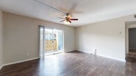 Located at 501 116th Ave N in Saint Petersburg, Florida, this single-floor residence offers a well-organized layout designed for comfortable everyday living. The main living area is finished with durable wood-style flooring that extends throughout the common spaces, lending a clean, cohesive look. A ceiling fan with a light fixture is centrally mounted beneath a textured ceiling, providing both airflow and ambient lighting. Sliding glass doors open to a private outdoor balcony enclosed by a wooden privacy fence, allowing natural light to fill the living space while offering a comfortable outdoor retreat. The kitchen features white cabinetry with ample storage, light countertops, and black appliances, including a full-size refrigerator. It connects seamlessly to the main corridor, which leads to the bedrooms and bathroom. The bedrooms are carpeted, creating a softer, quieter environment, and each room includes windows with blinds for natural light and privacy. Closet access is present in the bedroom area. The bathroom is fitted with wood-style flooring, a white vanity with storage, a tiled tub-shower combination, and clean, simple finishes throughout. Overall, the space presents a practical and functional layout suited to a variety of lifestyles in the heart of the Saint Petersburg area.