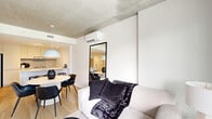Located at 120 Place Charles-Le Moyne in Longueuil, this well-appointed one-bedroom, one-bathroom unit showcases a clean, contemporary design with a cohesive palette of white and natural wood tones. Light hardwood flooring flows throughout, complementing the bright, minimalist aesthetic.

The open-concept kitchen is a standout feature, offering sleek flat-front white cabinetry extending to the ceiling, stainless steel appliances including a built-in oven and French door refrigerator, and a generous white waterfall island with an undermount sink — ideal for both cooking and casual dining with bar seating.

The bedroom is a calm retreat, highlighted by an exposed concrete ceiling that adds an industrial edge to the otherwise soft, neutral space. A large window frames views of the surrounding urban landscape, filling the room with natural light. A built-in closet provides practical storage.

The bathroom continues the minimalist theme with all-white wall and floor tiles, a soaker tub with shower, and clean-lined fixtures, creating a serene and functional space.

Compact yet efficiently laid out, this unit makes excellent use of its footprint, offering a cohesive living environment with modern finishes throughout.