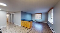 Located at 101 N Grant St in Denver's Capitol Hill neighborhood, this single-floor unit offers a functional and well-organized layout designed for comfortable city living. The kitchen is equipped with black appliances, including a full-size refrigerator, electric range, and microwave, all complemented by light wood cabinetry and tile flooring. A peninsula counter with a dark countertop and additional cabinetry beneath serves as a natural divider between the kitchen and the living area, which features hardwood-style flooring and a large window that fills the space with natural light and views of the surrounding neighborhood. The open layout creates a seamless flow between cooking and living spaces. Two bedrooms are finished with plush carpeting, ceiling fans, and individual wall-unit HVAC systems, each with windows that invite natural light and outdoor views of the tree-lined surroundings. The bathroom is thoughtfully appointed with tile flooring, a wood-trimmed vanity with a dark countertop, and a combination tub and shower equipped with safety grab bars for added accessibility. Throughout the unit, neutral wall tones provide a clean, versatile backdrop, while baseboard heating and wall-unit climate control ensure year-round comfort. The unit's location in Capitol Hill offers convenient access to Denver's vibrant dining, arts, and transit corridors.
