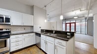 Located at 1278 West 9th Street in Cleveland's vibrant Ohio City neighborhood, this one-bedroom, two-bathroom unit offers an efficient and well-appointed layout across a single floor. The open-concept kitchen is a standout feature, boasting white shaker cabinetry, dark granite countertops, a classic subway tile backsplash, stainless steel appliances, and a peninsula with bar seating — all illuminated by modern pendant lighting. Warm hardwood floors run throughout the main living areas, complementing the industrial character of exposed ceiling beams and ductwork. A hallway connects the living spaces to the private quarters, where the spacious bedroom features plush carpeting, a built-in closet, and floor-to-ceiling vertical blinds framing access to an exterior balcony with natural light. The two bathrooms include granite or stone-style countertops, clean white fixtures, and a tub-shower combination. The unit also benefits from a ceiling fan and track lighting throughout. The overall ambiance blends urban loft aesthetics with practical residential comfort, making it a well-suited home in one of Cleveland's most walkable and dynamic neighborhoods.
