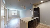 This single-story unit in Kyle, TX offers a clean, modern design with a cohesive neutral color palette throughout. The open-concept layout connects the kitchen and living area seamlessly, creating a bright and functional living space. The kitchen is a standout feature, equipped with dark espresso cabinetry, granite countertops, a peninsula with an undermount sink, pendant lighting, track lighting, and black appliances including a refrigerator, range, and dishwasher. Light wood-style plank flooring runs throughout the main living areas, adding warmth and continuity to the space. The living area benefits from natural light through a window fitted with blinds and is complemented by a ceiling fan overhead. A hallway leads to the private areas of the home, including multiple bedrooms, each finished with the same light wood-style flooring, ceiling fans, and windows that invite natural light. The bathroom features a full soaking tub with a built-in surround shelf system and dark cabinetry accents. Throughout the unit, neutral grey walls, recessed lighting, and clean white trim contribute to a contemporary and move-in-ready aesthetic, making this Kyle, TX residence an inviting and well-designed space.