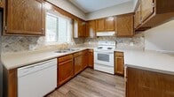 Located at 1250 5th St NE in Hickory, NC, this single-floor, 2-bedroom, 3-bathroom home offers a practical and comfortable layout across a well-utilized footprint. The kitchen is equipped with warm oak cabinetry, a tile backsplash, white appliances including a range, dishwasher, and refrigerator, and durable wood-look vinyl flooring. A peninsula counter connects the kitchen to the adjacent living room, which features rich dark hardwood-style flooring and a classic fireplace, creating an inviting focal point for the main living area. Natural light filters in through windows fitted with blinds. The two bedrooms are carpeted for comfort and each includes a ceiling fan. The spacious primary bedroom offers ample room and a louvered bi-fold closet. The additional bedroom also features wood-look flooring. Three bathrooms serve the home, each with warm oak vanities and matching flooring consistent with the rest of the unit. A hallway with a towel bar connects the private areas of the home. Neutral warm beige tones throughout the walls lend a cohesive, understated aesthetic. The home also includes a patio, providing an outdoor extension of the living space.