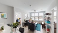 This contemporary single-floor unit offers a well-designed layout that balances communal living with private bedroom spaces. The open living area serves as the heart of the unit, featuring light wood-style flooring, a ceiling fan, and large windows fitted with horizontal blinds that allow generous natural light and views of the surrounding cityscape. The space is versatile and comfortable, accommodating both relaxing and entertaining.

The kitchen is thoughtfully outfitted with a two-tone cabinetry design — dark lower cabinets paired with crisp white upper cabinets — and light countertops. Stainless steel appliances, including a refrigerator, electric range, and built-in microwave, provide full functionality for everyday living.

The unit includes multiple bedrooms, each carpeted and equipped with a ceiling fan, and large windows that frame outdoor urban views. Each room offers a private, comfortable retreat within the shared living environment.

Two full bathrooms serve the unit, both featuring warm wood-toned vanity cabinetry, light countertops, large mirrors, and light wood-style flooring. One bathroom includes a shower-tub combination, while the other offers a walk-in closet adjacent to the vanity area. Neutral gray walls and consistent modern finishes create a cohesive, clean aesthetic throughout the entire space.