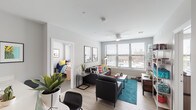 This contemporary single-floor unit offers a well-designed layout that balances communal living with private bedroom spaces. The open living area serves as the heart of the unit, featuring light wood-style flooring, a ceiling fan, and large windows fitted with horizontal blinds that allow generous natural light and views of the surrounding cityscape. The space is versatile and comfortable, accommodating both relaxing and entertaining.

The kitchen is thoughtfully outfitted with a two-tone cabinetry design — dark lower cabinets paired with crisp white upper cabinets — and light countertops. Stainless steel appliances, including a refrigerator, electric range, and built-in microwave, provide full functionality for everyday living.

The unit includes multiple bedrooms, each carpeted and equipped with a ceiling fan, and large windows that frame outdoor urban views. Each room offers a private, comfortable retreat within the shared living environment.

Two full bathrooms serve the unit, both featuring warm wood-toned vanity cabinetry, light countertops, large mirrors, and light wood-style flooring. One bathroom includes a shower-tub combination, while the other offers a walk-in closet adjacent to the vanity area. Neutral gray walls and consistent modern finishes create a cohesive, clean aesthetic throughout the entire space.