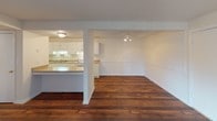 This single-floor residence offers a practical and comfortable layout designed for everyday living. The living area is a generous, open space highlighted by rich, dark hardwood flooring and a large sliding glass door fitted with vertical blinds, allowing abundant natural light to fill the room. Adjacent to the living area, the kitchen is efficiently designed with white cabinetry lining the walls, ample counter space, a double sink, and white appliances including a range and refrigerator. A pass-through counter connects the kitchen to the dining and living areas, creating a seamless, open-plan feel. The bedrooms are carpeted in neutral tones, providing warmth and comfort, and each room features windows with blinds that invite natural light. Textured ceilings are present throughout the space. The primary bedroom benefits from convenient access to a full bathroom and a walk-in closet, offering added functionality. Two full bathrooms serve the residence, each featuring a tiled tub-shower combination, toilet, and vanity. Throughout the home, a clean, neutral color palette of soft whites and beiges creates a cohesive and move-in-ready atmosphere suited to a variety of personal styles.