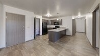 This single-floor residence offers a practical and comfortable layout across three bedrooms, one bathroom, a combined kitchen and living area, three closets, and a dedicated in-unit laundry room. The open-concept living and kitchen area serves as the heart of the home, featuring wood-style flooring that transitions to carpet in the living space. A sliding glass door fills the living room with natural light and provides access to an outdoor balcony, complemented by a ceiling fan and chandelier fixture overhead.

The kitchen is well-equipped with dark espresso cabinetry, light stone countertops, and a full suite of black appliances including a refrigerator, electric range with over-the-range microwave, and dishwasher. A peninsula with a built-in sink adds additional counter space and facilitates an open connection to the living area.

Each bedroom features plush carpeting and white walls. Two bedrooms include windows with outdoor views of open green space. The primary bedroom offers generous dimensions, while a third bedroom features exposed ductwork along the ceiling.

The bathroom is finished with large-format tile flooring, a dark vanity with light countertop, a full tub-shower combination, and chrome fixtures. The in-unit laundry area houses a full-size top-load washer and dryer with an overhead shelf for storage.