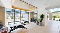 Located at 1000 Spring St NW in Atlanta's vibrant Midtown neighborhood, this two-floor fitness center spans an impressive total area across both levels, offering a thoughtfully designed environment for a wide range of workout activities. The facility features a modern, clean aesthetic with warm wood-paneled tray ceilings, recessed lighting, and resilient rubberized flooring throughout.

The lower level boasts soaring double-height ceilings and floor-to-ceiling glass walls that flood the space with natural light and provide open views of surrounding greenery. This floor houses a dedicated functional training area equipped with TRX suspension systems, a heavy punching bag, medicine balls, and free weights. A dramatic indoor bouldering wall serves as a striking focal point, accompanied by a rowing machine and open stretching areas. Glass-enclosed studio spaces feature an Echelon smart mirror for connected fitness classes.

The upper level offers a well-appointed strength and cardio zone, complete with cable machines, adjustable benches, extensive dumbbell racks, and a full row of treadmills lining a mirrored wall. Panoramic windows on this floor provide sweeping city views. A connecting staircase with a vibrant yellow-green railing ties both floors together seamlessly, creating a cohesive and energizing fitness environment.