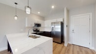 Located at 5711 Menerey Ln in Columbus, Ohio, this single-floor residence showcases a clean, modern design with contemporary finishes throughout. The open-concept kitchen serves as a centerpiece, featuring striking two-tone cabinetry with crisp white upper cabinets and dark espresso lower cabinets, complemented by a marble-look quartz waterfall peninsula with an undermount double sink. Stainless steel appliances — including a French door refrigerator with water dispenser, electric range, and built-in microwave — add a polished, functional appeal. A textured tile backsplash and pendant lighting complete the kitchen's refined look. Light-toned hardwood-style flooring flows seamlessly throughout the entire space, lending warmth and visual continuity. The bedroom is well-proportioned, featuring a ceiling fan, a window with natural light and outdoor views, and neutral toned walls that create a calm, restful atmosphere. The bathroom is generously sized, offering a wide vanity with a backlit mirror, white cabinetry with brushed gold hardware, a walk-in glass-door shower, and a separate toilet area. A stacked laundry closet is also conveniently located within the bathroom. The overall ambiance is bright, clean, and move-in ready, reflecting thoughtful modern design.