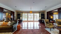 Located at 850 Toftrees Ave in State College, Pennsylvania, this single-floor clubhouse is a thoughtfully designed community space that blends eclectic style with functional versatility. A defining architectural feature throughout is the richly polished, deep-red stained concrete flooring, which lends a warm, upscale character to every room.

The main lounge area is expansive and light-filled, anchored by a sweeping wall of large-pane windows that frame views of the outdoor pool area and surrounding landscape. A statement pendant light hangs overhead, while dark wood built-in cabinetry and framed artwork add a refined, layered aesthetic. Adjacent seating areas offer comfortable arrangements with sofas, armchairs, and accent pieces styled in earthy, eclectic tones.

A cozy lounge room features a full brick accent wall with a fireplace, a wall-mounted television, and an boldly painted orange ceiling that adds dramatic warmth and personality to the space. Another area functions as a business and media center, with built-in shelving, workstations, shiplap wall paneling, and multiple televisions for resident use.

A rustic barn door marks the entrance to a casual sitting room complete with a chalkboard calendar wall and chess table. Additional rooms include a well-appointed office space with built-in cabinetry and a suite-style room with a sleeping area, dark ceiling, and plaid window treatments. Crown molding and recessed lighting are consistent throughout, reinforcing the polished, cohesive design of this community hub.