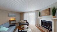 This single-story residence offers a functional and comfortable layout across several well-defined spaces. The living room serves as the focal point of the home, featuring wall-to-wall carpet, a textured ceiling, and a striking brick fireplace with a white mantel. A large sliding glass door fitted with vertical blinds allows abundant natural light to fill the room while providing outdoor access. The space is generously proportioned, lending itself to versatile furniture arrangements.

The galley-style kitchen is outfitted with white upper cabinetry, gray lower cabinets, and light countertops. Wood-look flooring runs throughout, complementing the black appliances, including a refrigerator, dishwasher, and range. A single-basin sink and ample storage make this an efficient cooking space.

Two carpeted bedrooms offer neutral tones and natural light through blinds-fitted windows, each providing a calm and adaptable retreat. The textured ceilings carry throughout these rooms, maintaining a consistent aesthetic.

Two bathrooms serve the residence. One features a shower stall with a glass sliding door, a single vanity, and wood-look flooring. The second bathroom includes a full tub-shower combination, matching vanity styling, and the same durable flooring, providing practicality and ease of maintenance throughout.