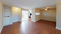 This well-appointed 2-bedroom, 2-bathroom residence offers a thoughtfully designed single-floor layout. The open living and dining area is highlighted by warm hardwood-style flooring, neutral beige walls, and a textured ceiling. A sliding glass door with vertical blinds connects the main living space to a private balcony, filling the room with natural light. The adjacent kitchen features white cabinetry with decorative raised paneling, granite-style countertops, black appliances including an electric range and dishwasher, and a pass-through opening to the living area. Both bedrooms are generously sized, each equipped with a ceiling fan and light kit, plush carpeting, and large windows dressed with blinds that invite ample natural light. The primary bathroom offers a double-sink vanity with granite-style countertops, white cabinetry, a full-width mirror, and a well-lit vanity bar. The second bathroom mirrors the same clean aesthetic with a single-sink vanity, matching countertops, and a framed mirror. The entry area features the same hardwood-style flooring as the main living space, contributing to a cohesive and polished look throughout the home.