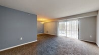 Located at 9100 Huntington Ct in Laurel, Maryland, this single-floor, 2-bedroom, 1-bathroom residence offers a comfortable and functional layout. The open living and dining area is generously sized, featuring plush dark carpeting, a tasteful blue accent wall, and a classic chandelier overhead. A large sliding glass door floods the space with natural light and provides direct outdoor access, making the living area feel bright and connected to the exterior.

The kitchen is well-appointed with warm honey-toned wood cabinetry, dark granite-style countertops, tile flooring, and black appliances including a full-size refrigerator, dishwasher, and range. A peninsula counter adds additional workspace and a natural division between the kitchen and the living area.

Both bedrooms are carpeted and offer a calm, neutral palette with ample natural light from vertical-blind-covered windows. The primary bedroom is notably spacious and includes access to a dedicated closet outfitted with built-in shelving rods for organized storage. The full bathroom features a clean white vanity with an under-cabinet storage unit, a bright mirror, and wood-look tile flooring. A hallway connects the rooms, completing this efficiently designed and move-in-ready home.