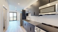 This 410 square foot apartment in Oakdale, MN, offers a modern and efficient living space. The single-floor layout maximizes functionality with a well-appointed kitchen, bathroom, and dedicated laundry area. The kitchen showcases sleek dark cabinetry contrasting with white subway tile backsplash and stainless steel appliances, including a refrigerator and range. Light-toned wood-look flooring flows throughout, enhancing the sense of space and continuity. The bathroom features a clean, minimalist design with a bathtub, toilet, and vanity. The laundry area is equipped with a stacked washer and dryer unit, optimizing space usage. Recessed lighting and a glass door in the kitchen area suggest attention to natural light. The overall design aesthetic is contemporary and cohesive, with a neutral color palette and streamlined fixtures. This apartment efficiently combines style and practicality in a compact urban living space.