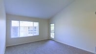 This single-floor residential space offers a clean, functional layout with a welcoming and understated aesthetic. The main living area is finished with wall-to-wall carpet in a neutral tone, providing a comfortable and quiet underfoot experience. Smooth, light-colored walls paired with white trim create a bright and airy atmosphere throughout the space.

Natural light is a defining feature of this room, with a large window fitted with horizontal blinds allowing for adjustable light control while framing views of the surrounding exterior. A glass-paneled door leads directly to a private balcony, further enhancing the sense of openness and providing additional ventilation and outdoor connectivity.

The ceiling is smooth and pitched slightly, adding subtle architectural interest and contributing to the overall sense of volume within the room. The space maintains a straightforward, move-in-ready condition with minimal ornamentation, allowing future occupants to personalize the interiors to their preference.

Overall, the space balances simplicity and practicality, making it well-suited for comfortable everyday living. The combination of soft carpeting, ample natural light, and direct outdoor access gives the space a relaxed and livable character.