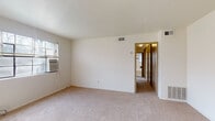 Located at 1750 Clifton Ave in Columbus, Ohio, this single-floor unit offers a straightforward, functional layout with a clean, neutral aesthetic throughout. The living area is generously proportioned, featuring wall-to-wall carpet in a warm beige tone and bright white walls that reflect natural light streaming in through blinds-equipped windows. A wall-mounted air conditioning unit and built-in floor vents provide climate control throughout the space. A hallway connects the living area to the remainder of the unit, with louvered bifold closet doors offering practical storage access along the corridor.

The kitchen is equipped with warm-toned wooden cabinetry, dark laminate countertops, a stainless steel sink, and a white gas range, providing a functional cooking environment. A full-size refrigerator is also included. The bedroom areas are carpeted and well-lit, each featuring windows with blinds that allow natural light to filter in, creating a bright and airy feel. One bedroom benefits from two windows, enhancing its sense of openness.

The bathroom retains a classic character with a black-and-white mosaic tile floor, white subway wall tiles accented with dark border tiles, a pedestal-style sink, a bathtub with shower, and a window for natural ventilation. Overall, the unit presents a clean, functional living environment.
