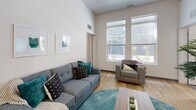 Located in Tampa, FL, this 4-bedroom, 4-bathroom unit is thoughtfully designed for shared living, offering each resident their own private bedroom, dedicated bathroom, and walk-in closet with built-in wire shelving. The open living area features soaring ceilings, large windows that invite abundant natural light, and wood-look flooring that flows seamlessly throughout the common spaces. A wall-mounted TV and comfortable seating make the living room an inviting place to relax or socialize. The kitchen is outfitted with stainless steel appliances — including a range, over-the-range microwave, and full-size refrigerator — paired with sleek grey cabinetry and clean white countertops, offering both style and functionality. Each bedroom provides a cozy, carpeted retreat with a built-in desk and window with views of lush greenery, ideal for studying or unwinding. The private bathrooms are finished in crisp white with wood-look tile flooring, full tub-shower combinations, and modern vanities. The neutral color palette and contemporary design elements throughout create a clean, cohesive aesthetic, making this unit a practical and comfortable home for multiple residents.