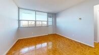 This efficiently designed 1-bedroom, 1-bathroom unit offers a thoughtful layout across a single floor, encompassing a living room, bedroom, kitchen, bathroom, and hallway. Polished parquet flooring in a classic herringbone-style pattern flows consistently throughout the living and sleeping areas, lending warmth and character to the space.

The living room is bright and airy, benefiting from a large window that invites natural light and frames views of the surrounding cityscape. The bedroom continues the same parquet flooring and features a floor-to-ceiling mirrored sliding closet, which enhances the sense of space, alongside a window offering additional natural light and outdoor views.

The kitchen is fitted with white cabinetry, granite-style countertops, a double stainless steel sink, and includes a stainless steel refrigerator — providing a clean, functional workspace. Tile flooring in the kitchen offers a practical contrast to the warm wood tones elsewhere.

The bathroom is a standout feature, finished with large-format marble-effect wall tiles surrounding a full soaking tub, accented by a band of metallic mosaic tiles that add a refined, contemporary touch. Neutral grey walls throughout the unit create a calm, cohesive palette, making this a well-rounded and move-in-ready space.