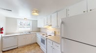 This two-floor townhome offers a straightforward, functional layout across multiple rooms designed for comfortable everyday living. The kitchen is outfitted with white cabinetry extending from base to ceiling, providing ample storage throughout. Light-toned laminate countertops offer generous prep space, while a white electric range, under-cabinet ventilation hood, and full-size refrigerator complete the appliance package. A tile backsplash lines the cooking area, and a window above the sink allows natural light to brighten the space. Tile flooring runs throughout the kitchen.

The living area is carpeted and features a large sliding glass door fitted with vertical blinds, opening to an outdoor view of greenery. The bedrooms are also carpeted, each featuring neutral wall tones and windows that bring in natural light and exterior views. The rooms are well-proportioned and versatile in their use.

Two bathrooms serve the townhome. One includes a tiled tub-and-shower combination with a marble-style vanity countertop and mirror. The second features a standalone shower with a frosted glass door and classic white subway tile wainscoting. Both bathrooms maintain a clean, utilitarian aesthetic consistent with the overall character of the home.