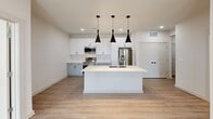 Located at 110 Frem Boustany Dr in Lafayette, Louisiana, this well-appointed 2-bedroom, 2-bathroom residence offers a thoughtfully designed single-floor layout with a clean, contemporary aesthetic throughout. Light wood-style flooring and a crisp white palette create a bright, cohesive atmosphere from room to room.

The kitchen serves as a central gathering point, anchored by a large white island with an undermount sink and striking trio of black pendant lights overhead. White upper cabinetry contrasts with gray lower cabinets, while a chevron-patterned tile backsplash adds visual texture. Stainless steel appliances complete the modern look. Recessed lighting illuminates the open living area adjacent to the kitchen.

Both bedrooms are well-lit, featuring large windows with blinds that invite natural light and offer views of the surrounding neighborhood. The primary bedroom includes a ceiling fan and a cozy nook, while the second bedroom is similarly bright and airy.

Each bathroom is finished with white cabinetry, white countertops, and black hardware accents, maintaining design consistency throughout. One bathroom includes built-in open shelving for additional storage. The hallway connects all areas efficiently, and a private balcony provides outdoor access. The overall ambiance is modern, clean, and move-in ready.