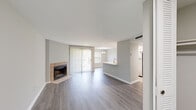 This single-floor residence offers a clean, modern aesthetic throughout, highlighted by consistent gray-toned hardwood-style flooring that flows seamlessly across the main living areas. The open-concept living and dining space is a standout feature, anchored by a tile-surround fireplace and framed by a large sliding glass door dressed with vertical blinds, allowing generous natural light to fill the room. A neutral color palette of soft grays and crisp white trim lends the space a calm, contemporary feel.

The kitchen is efficiently designed with white cabinetry, light countertops, a tile backsplash, and a full suite of stainless steel appliances including a refrigerator, range, and microwave. A peninsula with a sink opens toward the living area, enhancing the connected flow of the space.

The bedroom offers plush carpeting, a large window with slatted blinds overlooking greenery, and ample wall space for furnishings. The bathroom includes a full tub-shower combination with white tile surround and chrome fixtures. A dedicated in-unit laundry area accommodates a full-size washer and dryer, adding everyday convenience. Overall, the space presents a well-maintained, move-in-ready environment with practical features throughout.