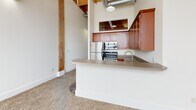 Located at 311 SW Water St in downtown Peoria, Illinois, this one-bedroom, one-bathroom loft delivers a distinctive industrial aesthetic rooted in its historic building origins. The space is defined by prominent exposed brick walls, warm wood beam ceilings with visible timber framing, and exposed ductwork — architectural elements that lend authentic character throughout.

The entrance leads through a carpeted hallway past a dedicated closet, opening into the combined dining and living area. Large windows allow natural light to fill the space, offering views of the surrounding area. The kitchen is efficiently designed with rich cherry wood cabinetry, a neutral stone-toned countertop that extends into a peninsula breakfast bar, stainless steel appliances including a refrigerator, range, and dishwasher, and tile flooring — all set against a striking exposed brick backdrop.

The bedroom is a well-proportioned retreat featuring carpet flooring, exposed brick accent walls, and a built-in storage cabinet. The bathroom continues the industrial aesthetic with exposed brick, a rustic timber post accent, tile flooring, and a full tub-shower combination. This loft offers a compelling blend of historic industrial design and functional modern living in the heart of Peoria.