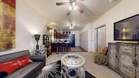 Located at 401 W Covell Rd in Edmond, Oklahoma, this one-bedroom, one-bathroom residence offers a thoughtfully designed single-floor layout that maximizes every inch of its compact footprint. The open-concept living and kitchen area serves as the heart of the home, featuring vaulted ceilings with ceiling fans that enhance the sense of airiness and space. Large windows allow natural light to fill the living room, which offers comfortable carpet flooring and direct sightlines to the kitchen. The kitchen is well-equipped with rich, dark cabinetry, black appliances including a refrigerator and range, granite-style countertops, and a breakfast bar with bar seating — ideal for casual dining. Wood-look flooring anchors the kitchen area, creating a clear visual distinction from the carpeted living space. The bedroom is a private retreat of comfortable size, featuring a ceiling fan, a large window with natural light, and generous closet space provided by dual bi-fold closet doors. A dedicated hallway connects the bedroom to the full bathroom, which features a dark wood vanity, a framed mirror, and ample lighting. The overall ambiance is warm and functional, with a layout that balances open communal living with private bedroom space.