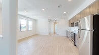 Located at 1001 Westwind St in Livermore, CA, this single-floor unit showcases a clean, contemporary design with an open-concept living and kitchen area. Light hardwood-style flooring runs throughout the main living spaces, contributing to a bright and airy atmosphere complemented by recessed lighting and white walls.

The kitchen is well-appointed with warm wood-toned cabinetry extending to the ceiling for ample storage, stainless steel appliances including a refrigerator, electric range, microwave, and dishwasher, and light-colored countertops. The layout flows seamlessly into the open living area, making the space feel expansive and connected. A dedicated laundry area with a stacked washer and dryer is also present.

The bedrooms feature soft neutral carpeting, large windows that invite natural light and views of the surrounding neighborhood, and closet space. One bedroom includes an attached area that leads to additional amenities.

The bathroom is finished in a modern style with a wood-toned vanity, white quartz countertop, an oversized mirror, and a full tub-shower combination, maintaining the unit's consistent contemporary aesthetic throughout.